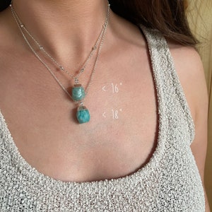 May include: Two silver necklaces with turquoise-colored gemstone pendants. The necklaces are layered, with one approximately 16 inches and the other 18 inches in length. The gemstones have a faceted, geometric shape, and the chains have small, round beads.