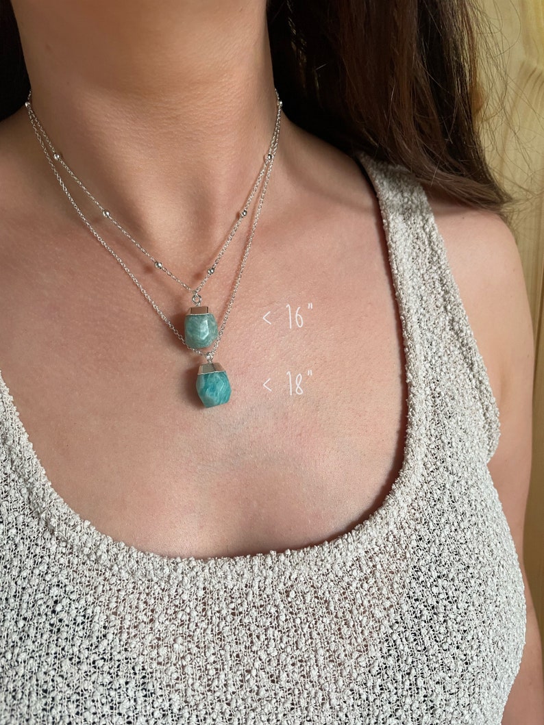 May include: Two silver necklaces with turquoise-colored gemstone pendants. The necklaces are layered, with one approximately 16 inches and the other 18 inches in length. The gemstones have a faceted, geometric shape, and the chains have small, round beads.