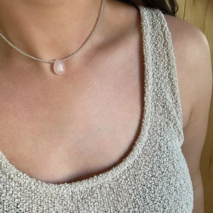 May include: A silver chain necklace with a light pink teardrop-shaped gemstone pendant.