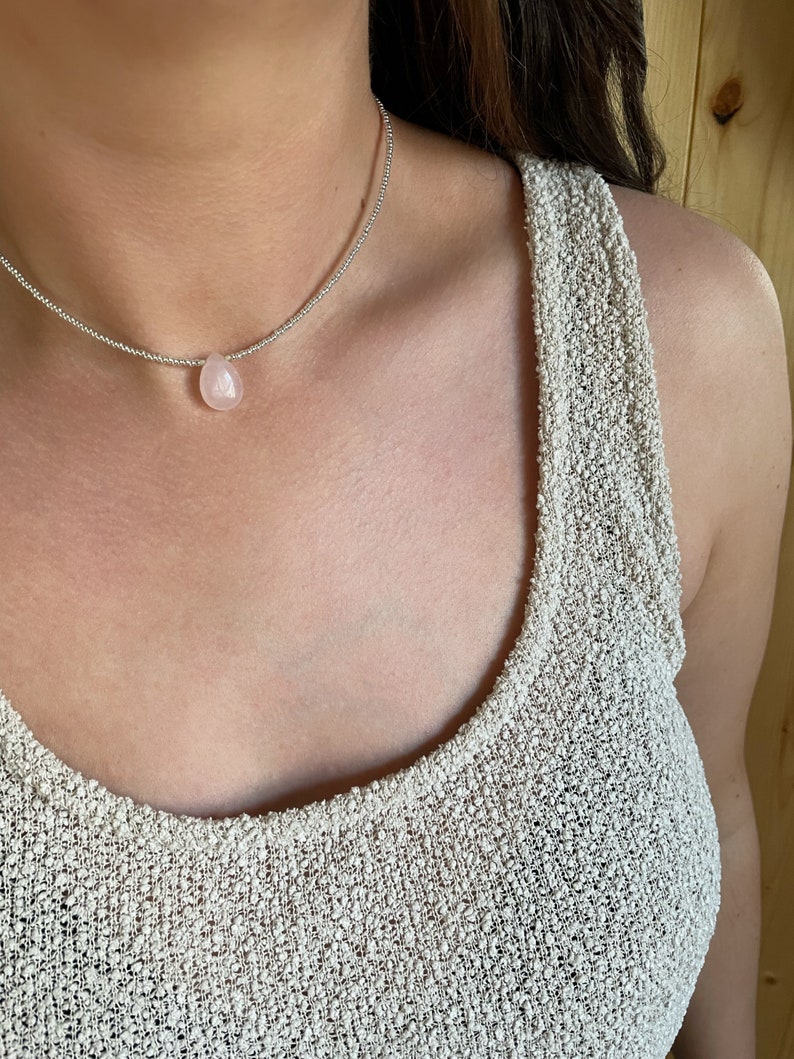 May include: A silver chain necklace with a light pink teardrop-shaped gemstone pendant.