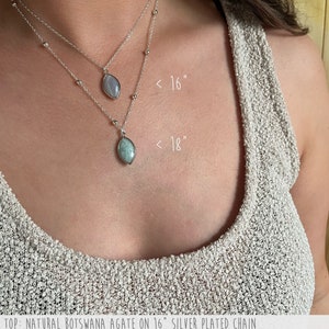 May include: Two silver necklaces with gemstone pendants. The top necklace features a Botswana agate pendant on a 16-inch chain. The bottom necklace has an amazonite pendant on an 18-inch chain. Both necklaces are silver-plated.