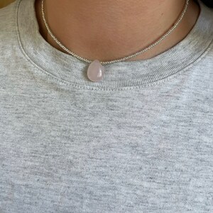 May include: A silver beaded choker necklace with a light pink teardrop-shaped pendant.