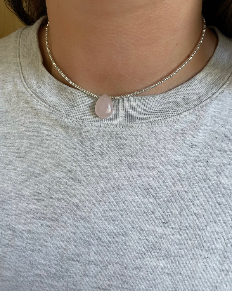 May include: A silver beaded choker necklace with a light pink teardrop-shaped pendant.