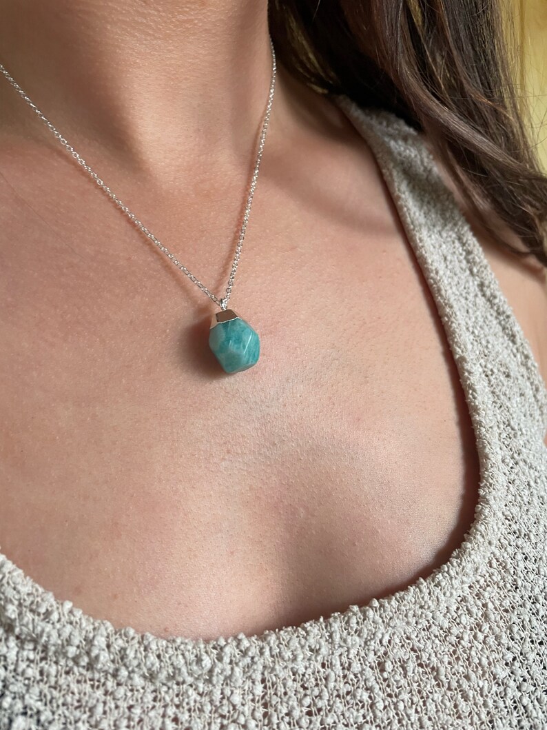 May include: A silver necklace featuring a faceted, light blue-green gemstone pendant. The pendant is a unique, irregular shape, and the chain is delicate. The necklace is displayed against a neutral background, highlighting the gemstone's color and texture.