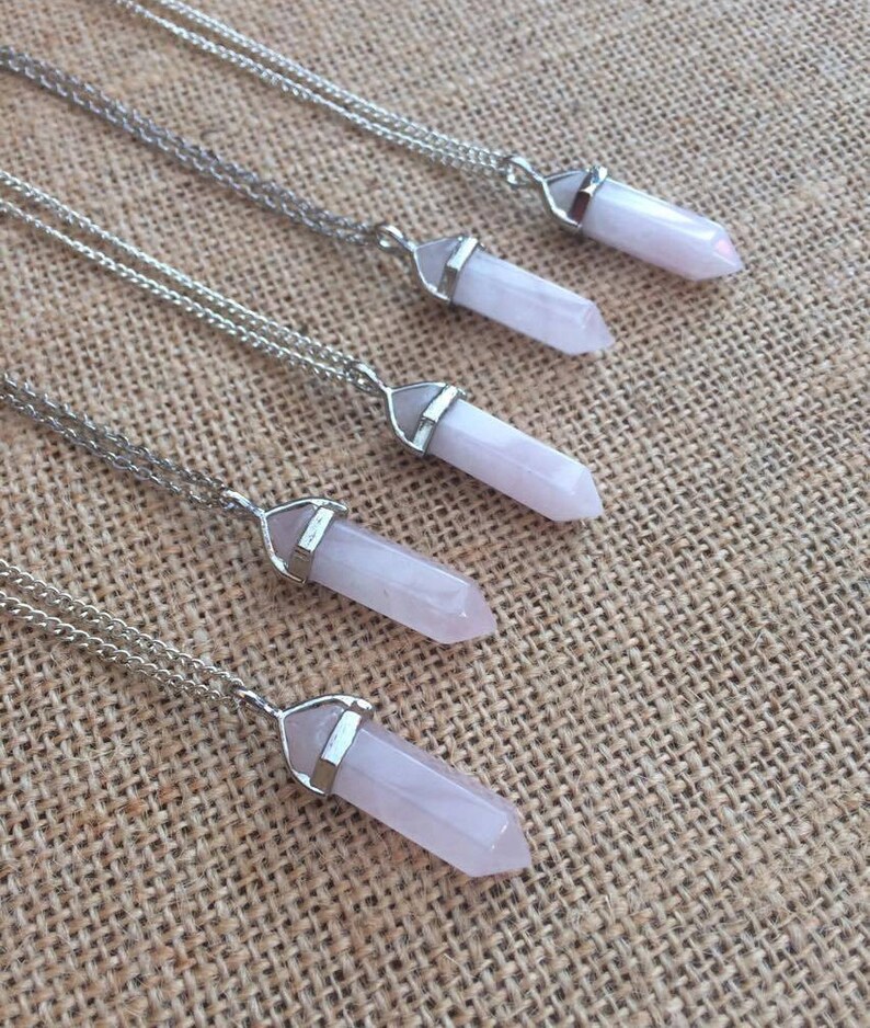 May include: Four silver necklaces with pink crystal point pendants. The necklaces are layered on a brown burlap background.