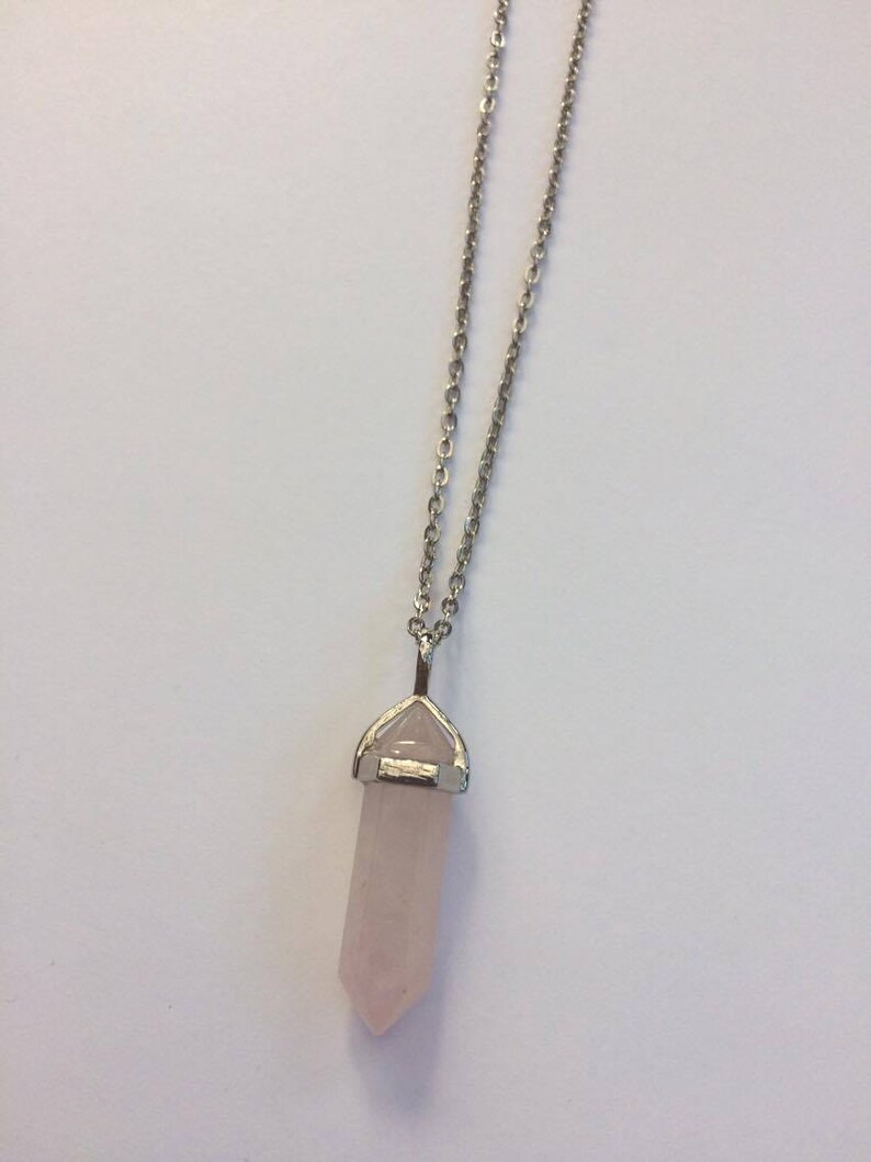 May include: A silver chain necklace with a rose quartz crystal pendant. The crystal is shaped like a point and is set in a silver bezel.