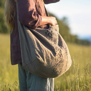 Può includere: Una persona che indossa una camicia marrone e jeans blu porta una grande borsa tote in tela marrone con un motivo floreale.