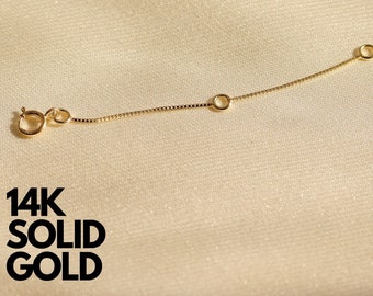 May include: A 14K solid gold necklace extender chain featuring a delicate box chain design, a circular spring ring clasp at one end, a small jump ring at the other, and an additional circular ring positioned along the length of the chain.