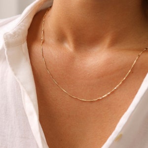 Pu&ograve; includere: Una delicata collana a catena d'oro con un designo semplice e discreto. La catena &egrave; realizzata con piccoli anelli piatti leggermente intrecciati.