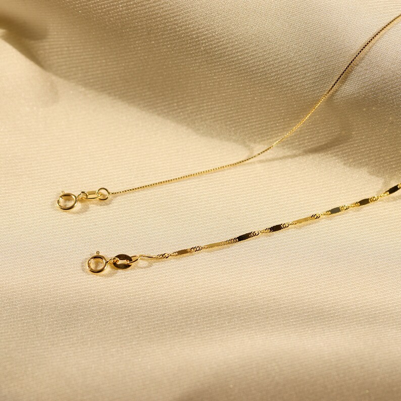 Pu&ograve; includere: Due catene d'oro, una con un design a catena a scatola e l'altra con un design a maglia piatta rettangolare. Entrambe le catene hanno una chiusura a moschettone.