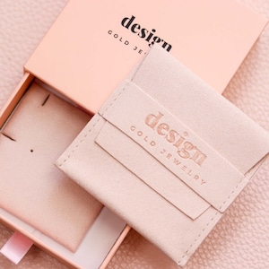 May include: A light pink jewelry box with a light pink suede pouch inside. The pouch has the text "design gold jewelry" embossed on it.