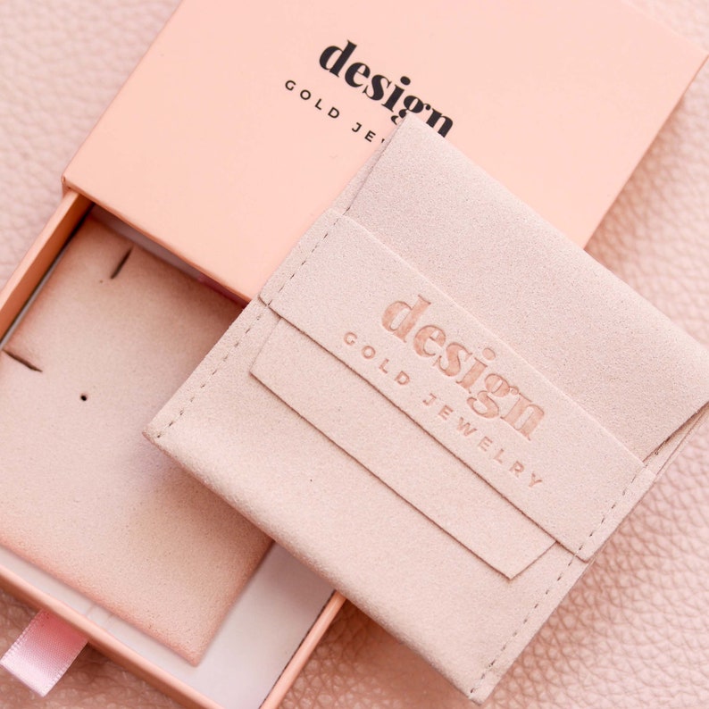 May include: A light pink jewelry box with a light pink suede pouch inside. The pouch has the text "design gold jewelry" embossed on it.