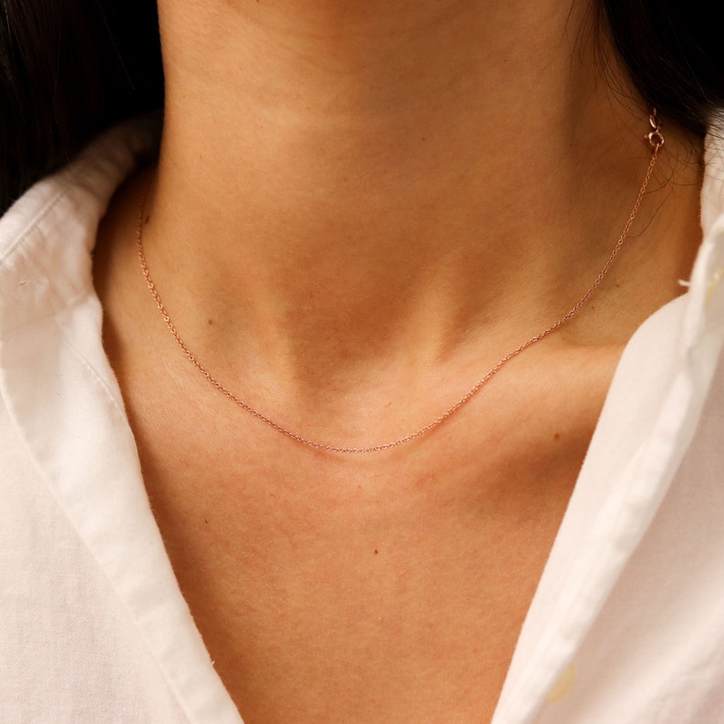 May include: A delicate rose gold chain necklace on a model wearing a white shirt.