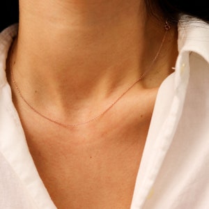 May include: A delicate rose gold chain necklace on a person's neck. The chain is thin and simple, and it is worn against a white shirt.