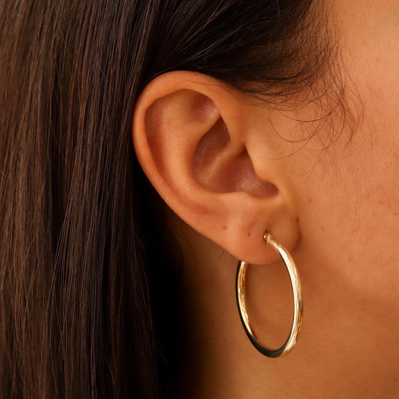 May include: A pair of gold hoop earrings worn in a person's ear.