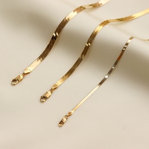 May include: Three gold snake chains of varying lengths, each with a lobster clasp closure.