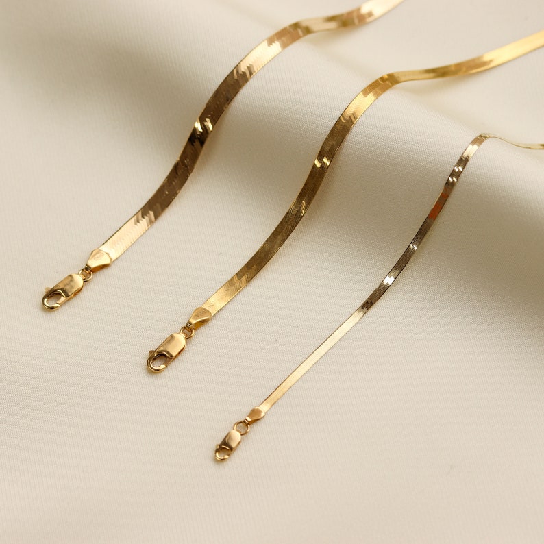 May include: Three gold snake chains of varying lengths, each with a lobster clasp closure.