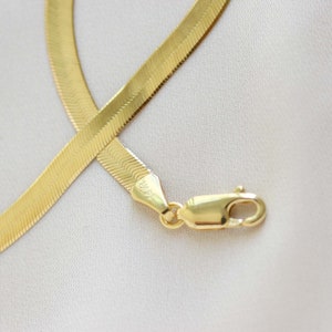 May include: A gold chain necklace with a herringbone pattern and a lobster clasp.