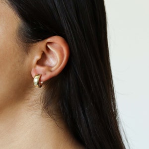 May include: A close-up of a person's ear wearing a pair of gold hoop earrings. The earrings are simple and elegant, with a smooth, polished finish.