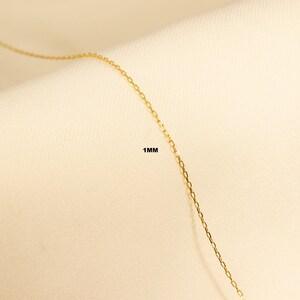 May include: A close-up of a gold chain necklace with a 1 mm width. The chain is made of small, linked squares.