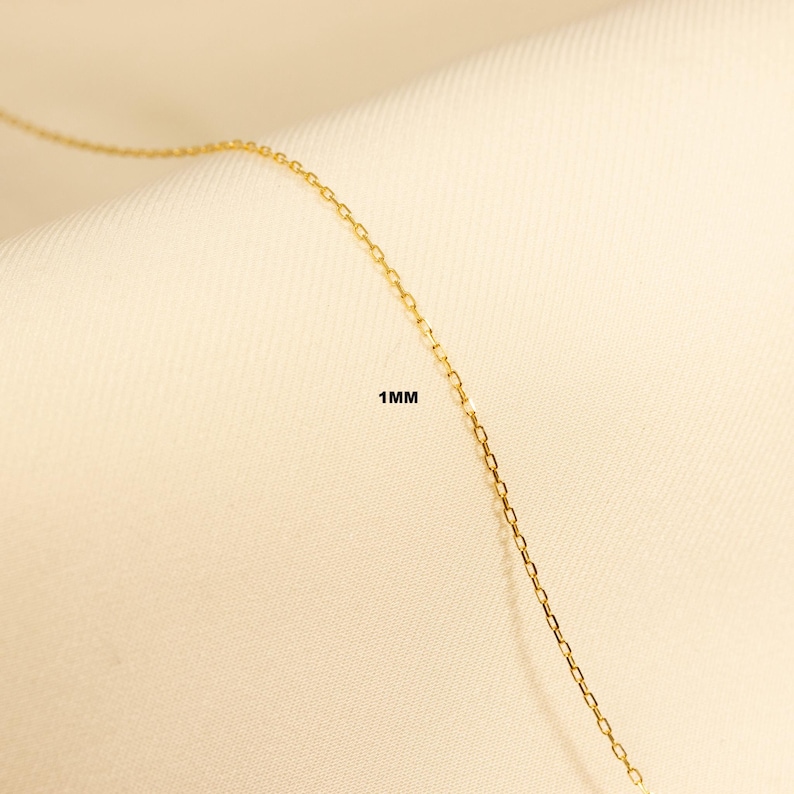 May include: A close-up of a gold chain necklace with a 1 mm width. The chain is made of small, linked squares.