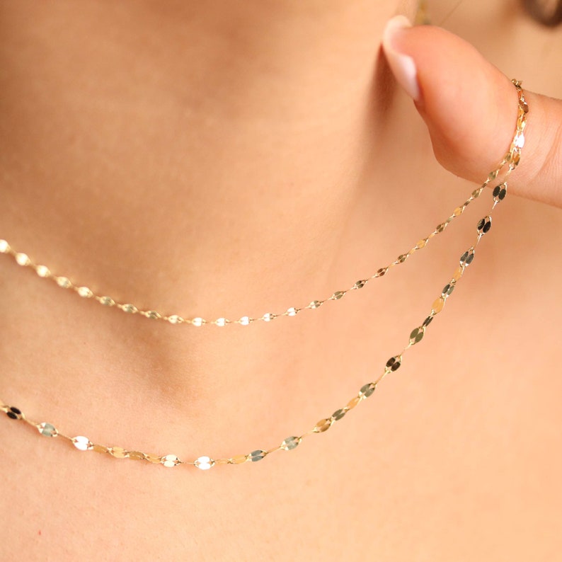 Puede incluir: Un delicado collar de cadena de oro con un dise&ntilde;o en capas. La cadena est&aacute; hecha de peque&ntilde;os eslabones ovalados.