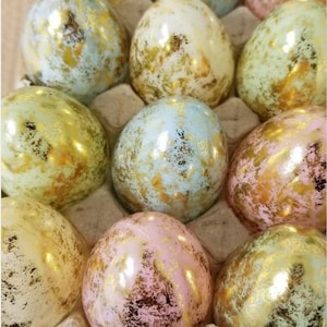 May include: A dozen pastel-colored Easter eggs with gold accents. The eggs are arranged in a carton and have a speckled, marbled appearance.
