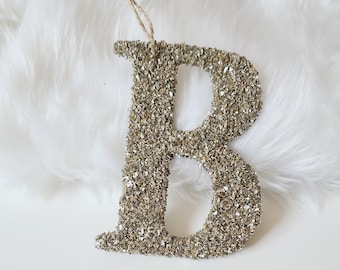 May include: A gold glitter letter B ornament with a string loop for hanging.