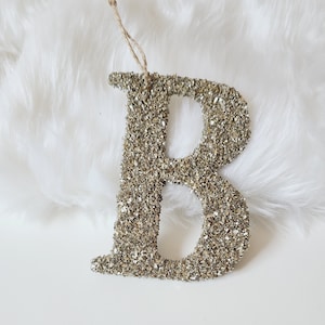 May include: A gold glitter letter B ornament with a string loop for hanging.