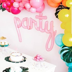 May include: A party-themed display with pink balloons, a pink balloon banner spelling "party", and a table with cupcakes, a cake, and macarons. The color scheme is pink, yellow, and teal.