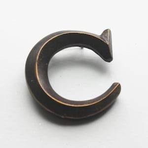 May include: A dark brown metal letter C with a slightly rounded shape.