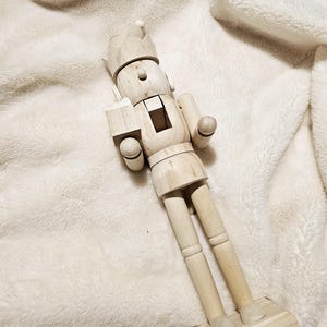 May include: A wooden nutcracker figurine with a crown, a mustache, and a painted face. The nutcracker is standing on a wooden base.