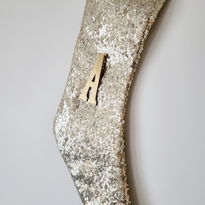 May include: Gold sequin Christmas stocking with a wooden letter A attached to the front.
