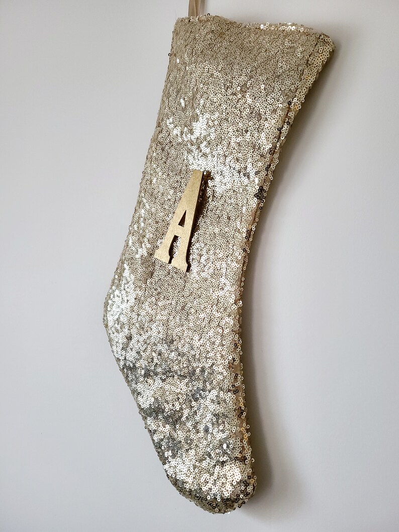 May include: Gold sequin Christmas stocking with a wooden letter A attached to the front.