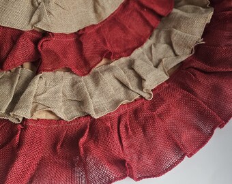 May include: A layered, ruffled tree skirt in alternating bands of red and tan burlap. The skirt has a circular shape with a textured, woven appearance. The ruffles add a decorative element to the design.