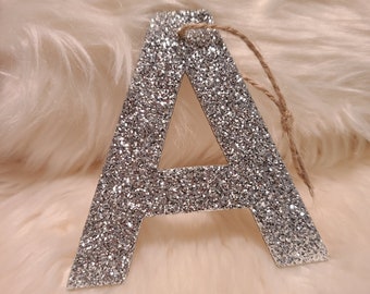 May include: A silver glitter letter A ornament with a brown twine string attached.