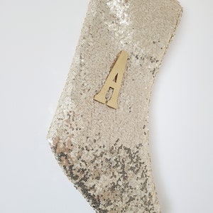 May include: A gold sequin Christmas stocking with a wooden letter "A" attached to the front.