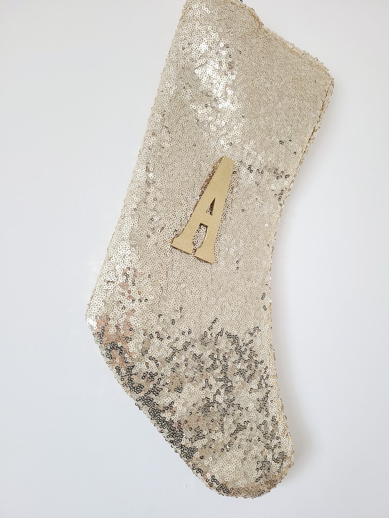 May include: A gold sequin Christmas stocking with a wooden letter "A" attached to the front.