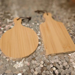 May include: Two wooden cutting boards, one round and one rectangular, with a light brown color and a natural wood grain. The boards are made of bamboo and have a smooth surface.