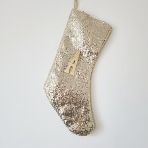 May include: Gold sequin Christmas stocking with a wooden letter A attached to the front.