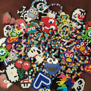 May include: A collection of colorful beaded bracelets with pixelated character designs, including Mario, Pac-Man, and other popular video game characters.