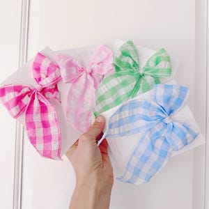 Op de afbeelding: Drie gingham lint haar strikken in roze, groen en blauw. De strikken zijn in een eenvoudige knoop geknoopt en klaar om te dragen.