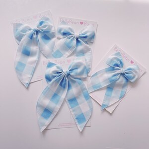 May include: Four blue and white gingham ribbon hair bows on white cards with the text "Bella Bean Bows" printed on them.