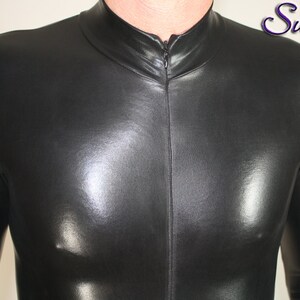 Op de afbeelding: Een zwarte, nauwsluitende bodysuit met een hoge kraag en een ritssluiting aan de voorkant. Het glanzende materiaal reflecteert licht, waardoor highlights en schaduwen ontstaan. Het Suzi Fox .com logo is zichtbaar.