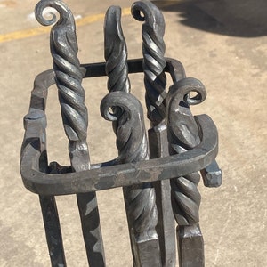 May include: A set of five black metal fireplace tools with twisted handles and decorative scrollwork. The tools are held in a black metal stand.