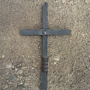 May include: A black metal cross with a twisted stem. The cross is made of wrought iron and has a simple, elegant design.