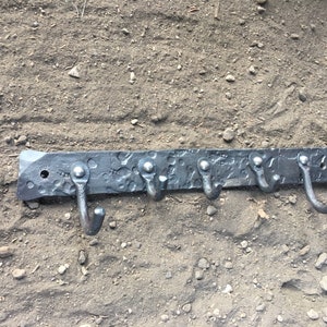 Puede incluir: Un colgador de metal negro con cinco ganchos. El colgador tiene una textura martillada y está montado en una pared.