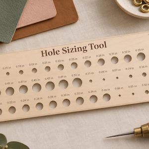 May include: A rectangular light-coloured wooden hole sizing tool featuring rows of circular cutouts of varying diameters, each labelled with its specific measurement in inches, ranging from 0.05 in to 0.51 in, with the text Hole Sizing Tool printed at the top.
