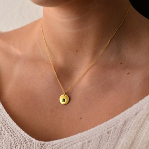 Könnte beinhalten: Eine goldene Kettenkette mit einem kleinen runden Anhänger mit dem Pausensymbol.