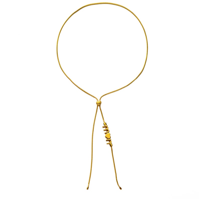 K&ouml;nnte beinhalten: Eine goldene Kettenkette mit einem verstellbaren Schiebeverschluss. Die Kette hat einen Herzanh&auml;nger mit dem Wort "MOM" in goldenen Buchstaben.